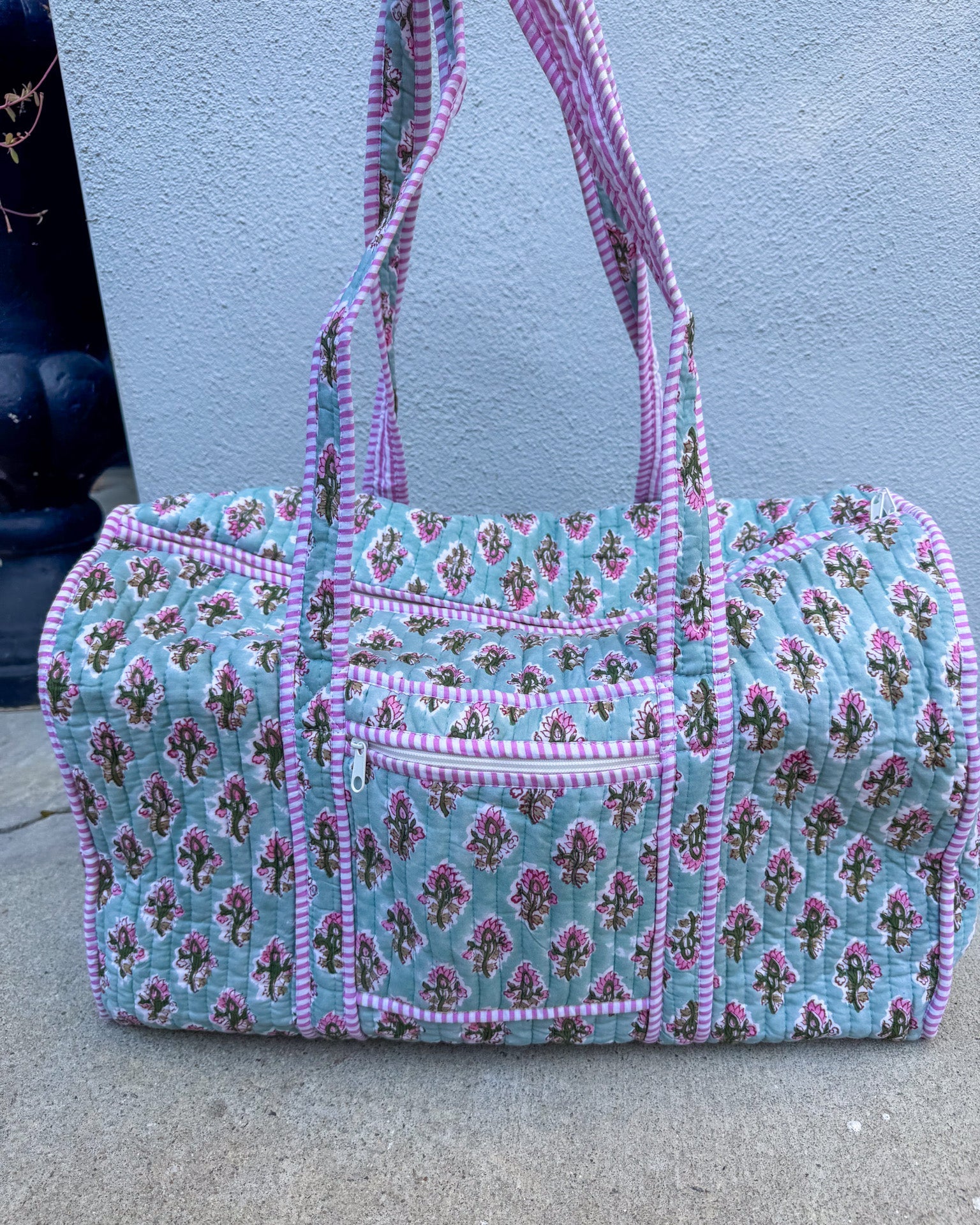 Floral patterned handbag with pink accents on a concrete surface.