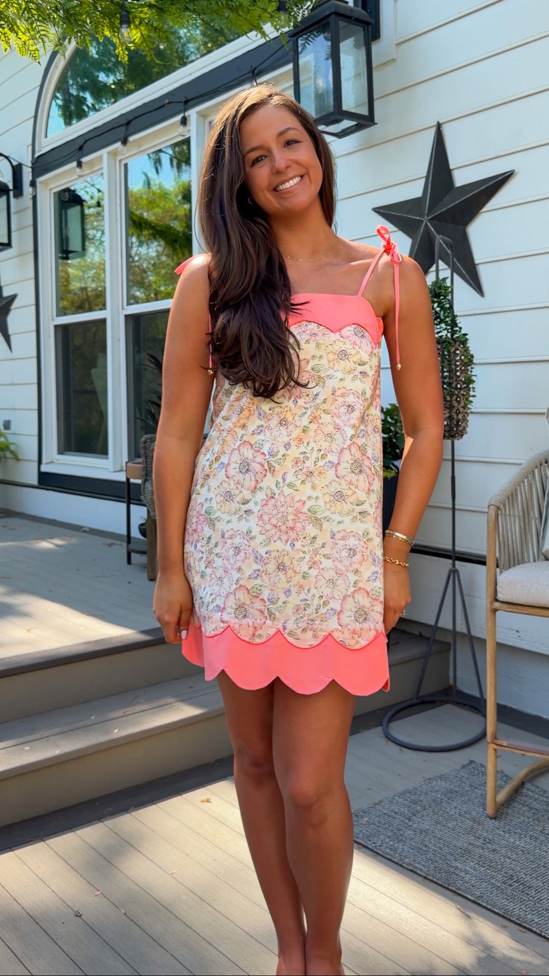 Woman wearing a floral dress with a pink bottom on a porch.