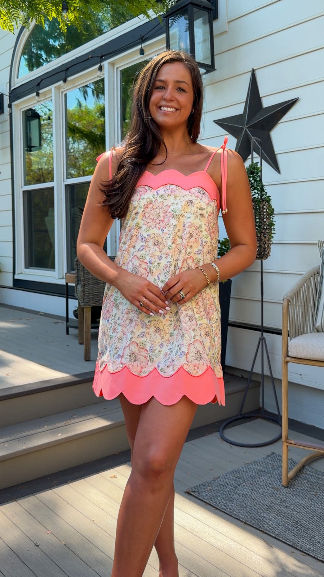 Woman in a floral dress standing on a porch with decorative stars and plants.