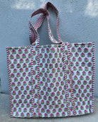 Floral patterned tote bag with striped handle against a textured wall.