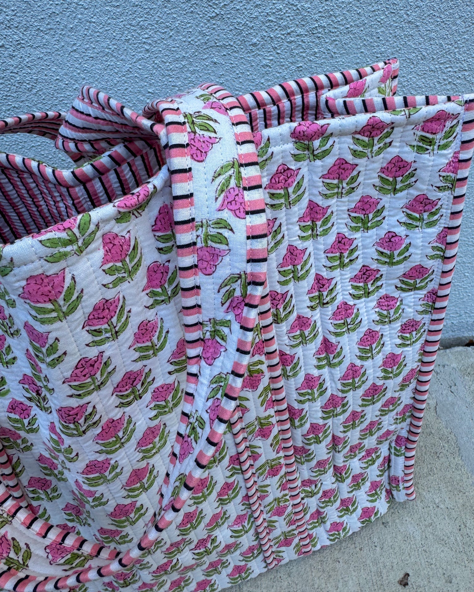 Floral-patterned fabric with pink flowers and green leaves on a white background, folded and leaning against a blue wall.