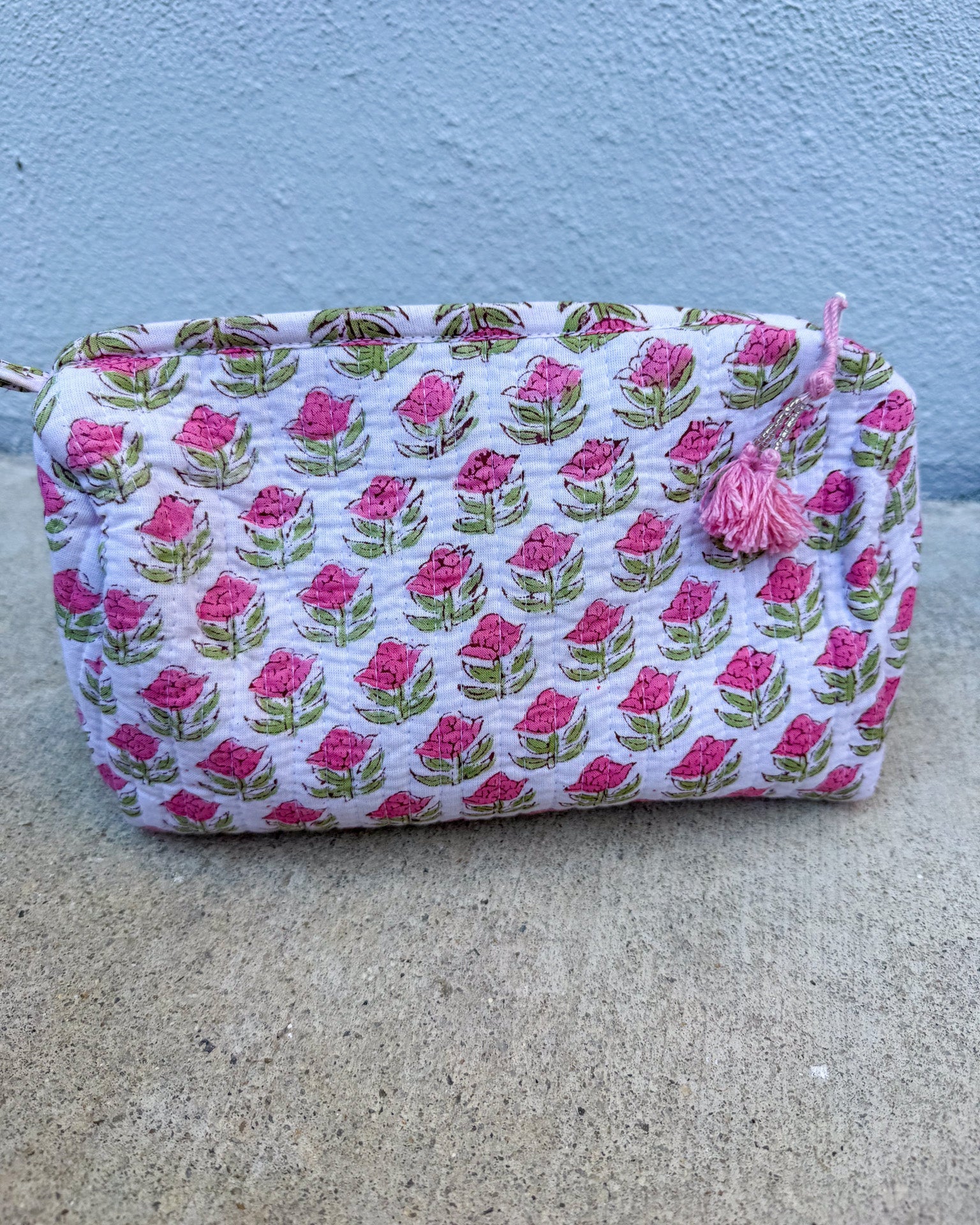 Fabric pouch with pink floral pattern on a concrete surface and blue wall background