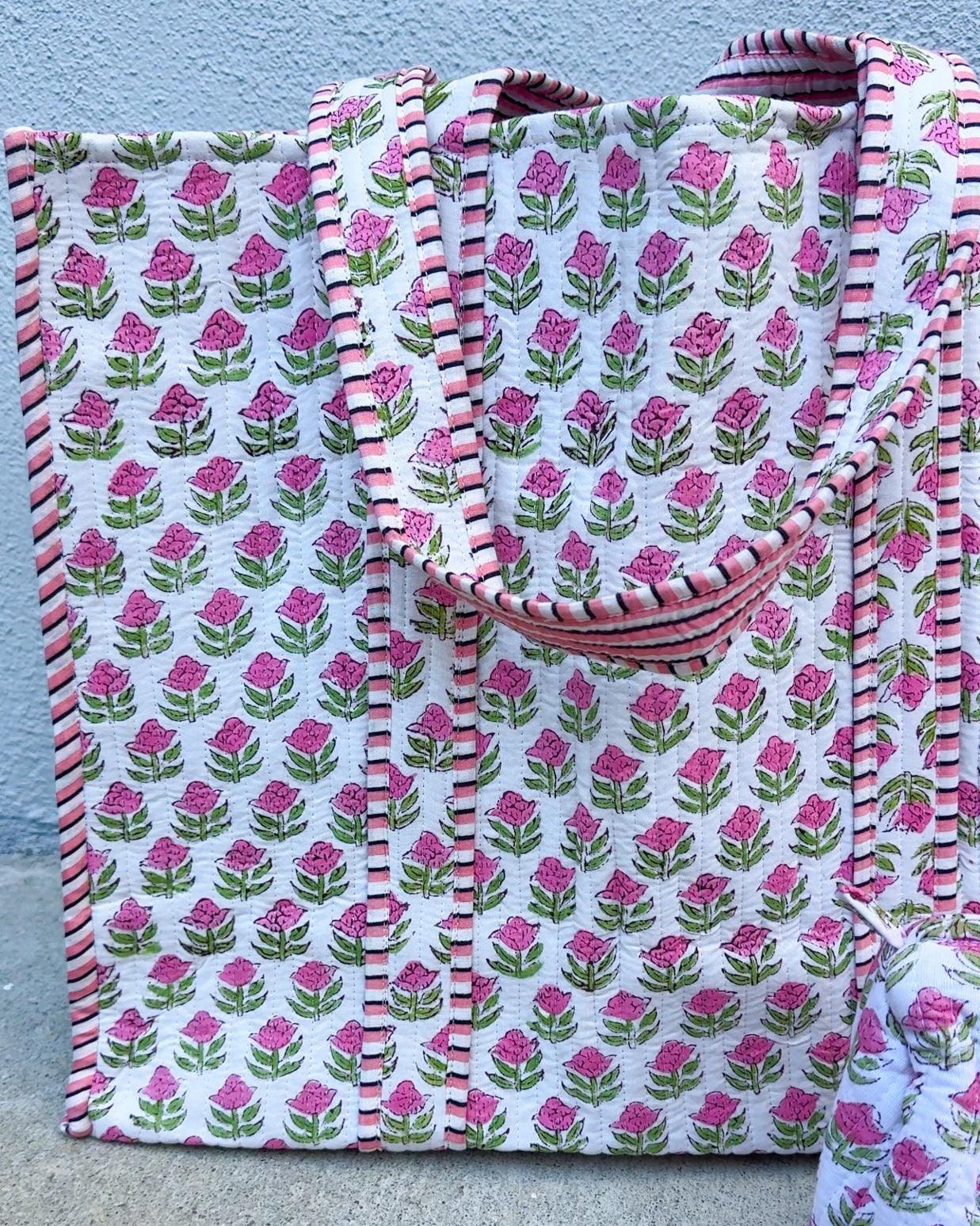 Floral patterned fabric with pink and green flowers on a white background, folded and displayed against a light blue wall.