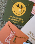 Gold necklace with a smiley face pendant on a textured surface with motivational cards.