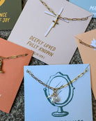 Gold necklace with a cross pendant on a card with text and other cards in the background.