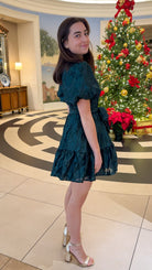 Hunter green floral textured mini dress with puff sleeves, covered button details, tie waist, and tiered skirt.