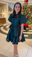 Hunter green floral textured mini dress with puff sleeves, covered button details, tie waist, and tiered skirt.