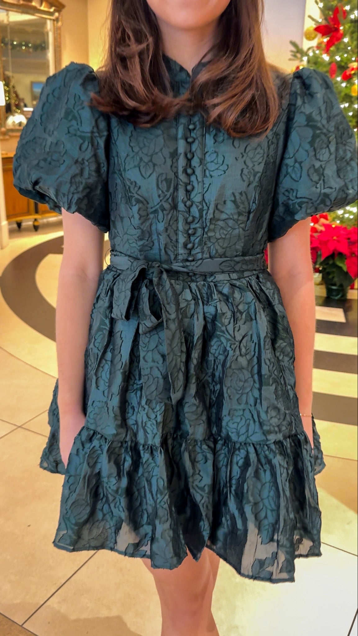 Hunter green floral textured mini dress with puff sleeves, covered button details, tie waist, and tiered skirt.