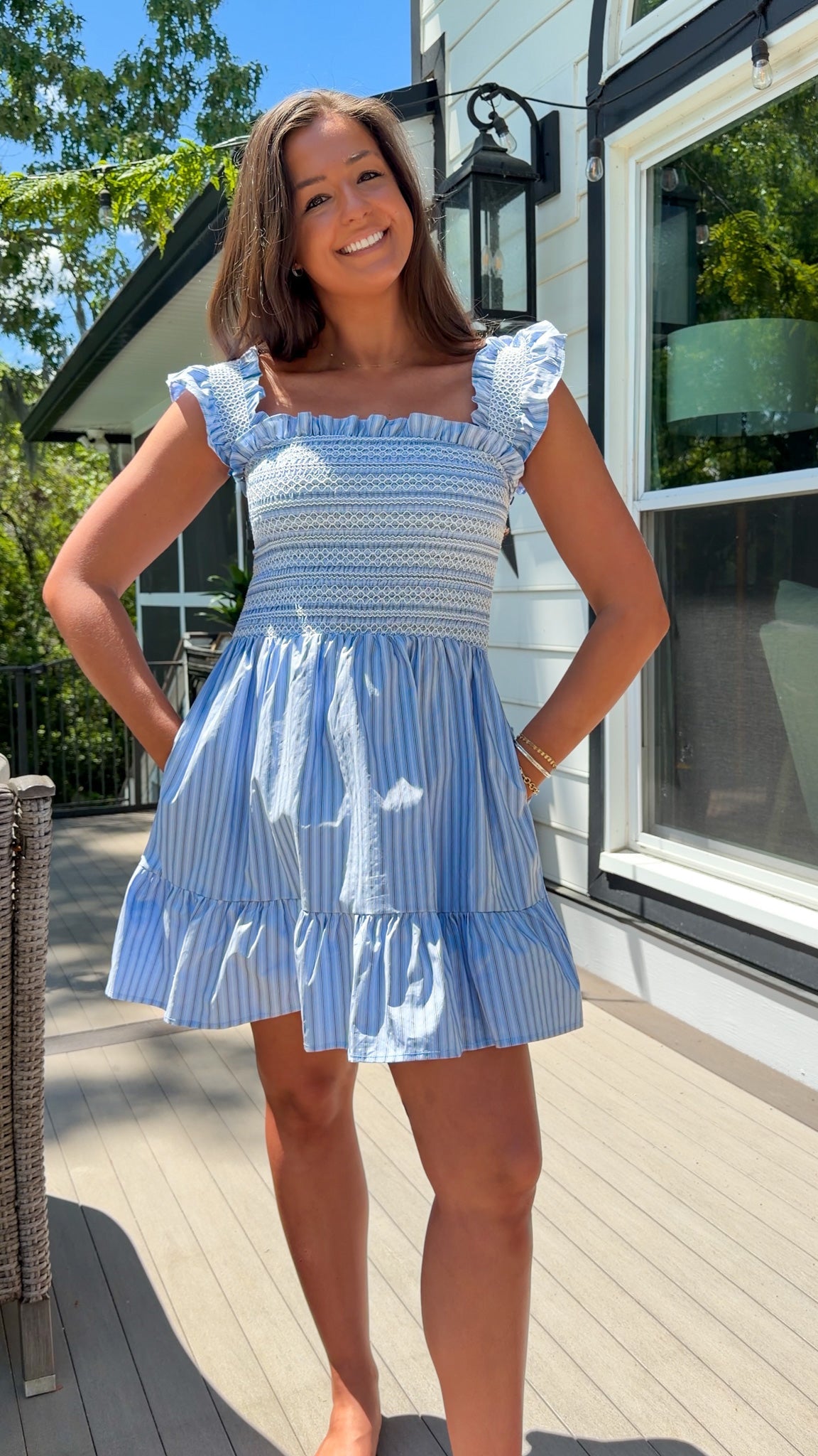 Woman wearing a blue and white dress standing on a deck with a house in the background