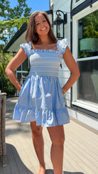 Woman wearing a blue and white dress standing on a deck with a house in the background