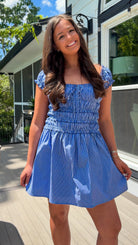 Woman wearing a blue dress standing outdoors on a wooden deck.