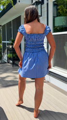 Woman in a blue dress standing on a wooden deck with a house in the background
