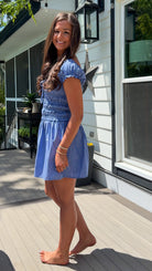 Woman in a blue dress standing on a wooden deck outside a house.