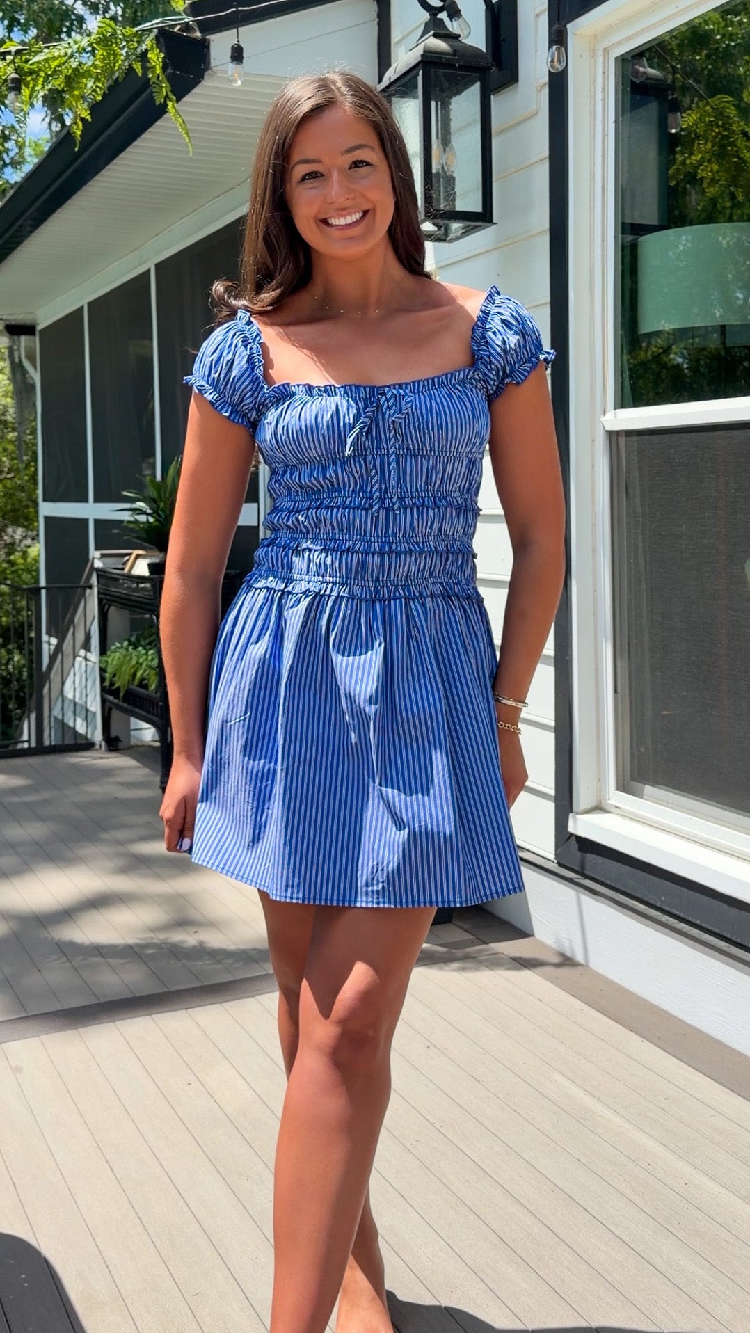 Woman in a blue dress standing on a wooden deck with a house in the background