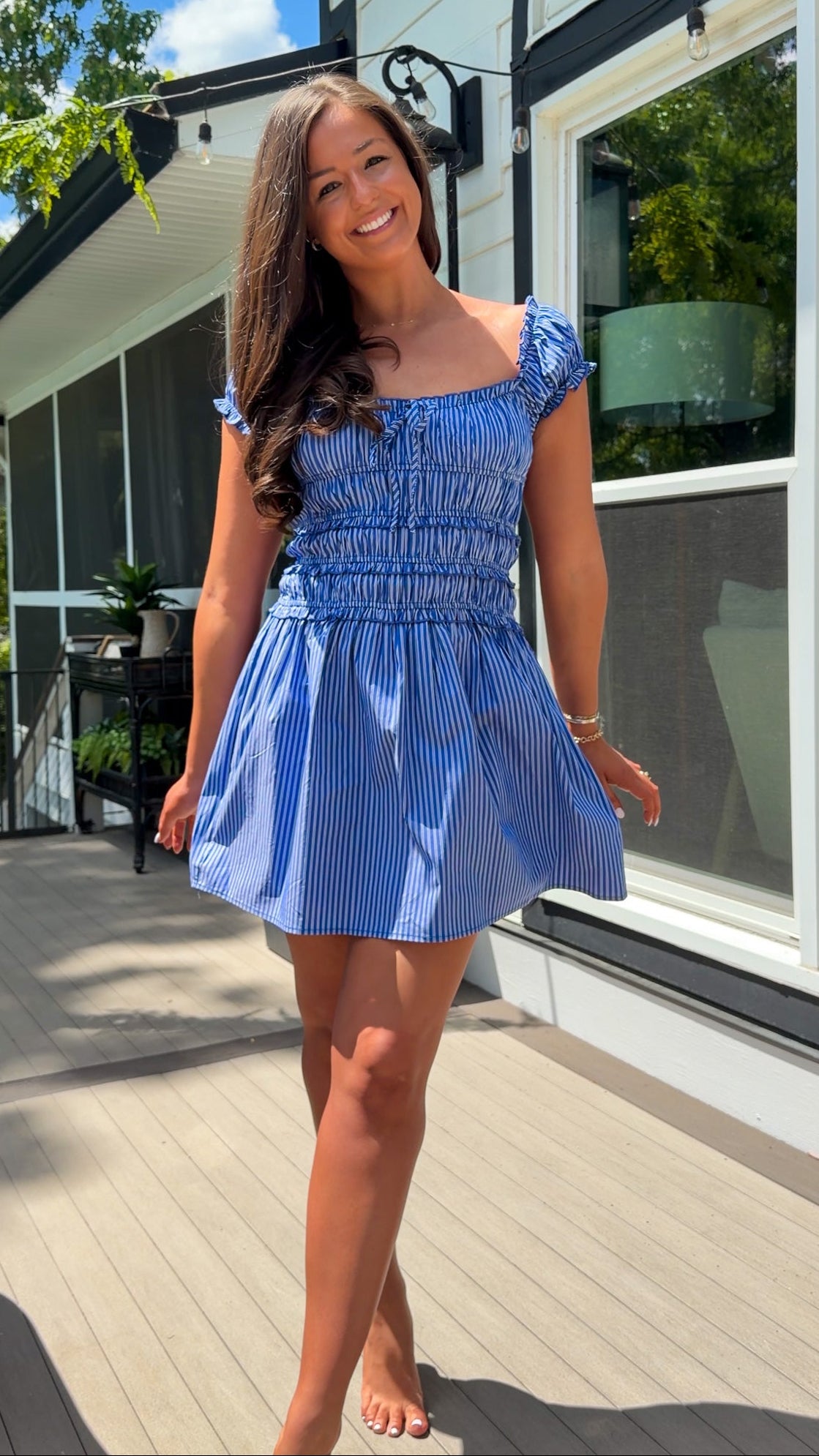 Woman in a blue dress standing on a wooden deck with a house in the background
