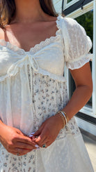 cream floral mini dress with eyelet lace, puff sleeves, scalloped neckline, and front tie detail