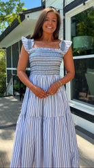 Woman in a blue and white striped dress standing outdoors near a house.