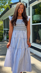 Woman wearing a blue and white striped dress standing outside a house.