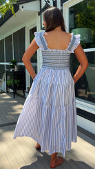 Woman in a blue and white striped dress standing on a wooden deck.