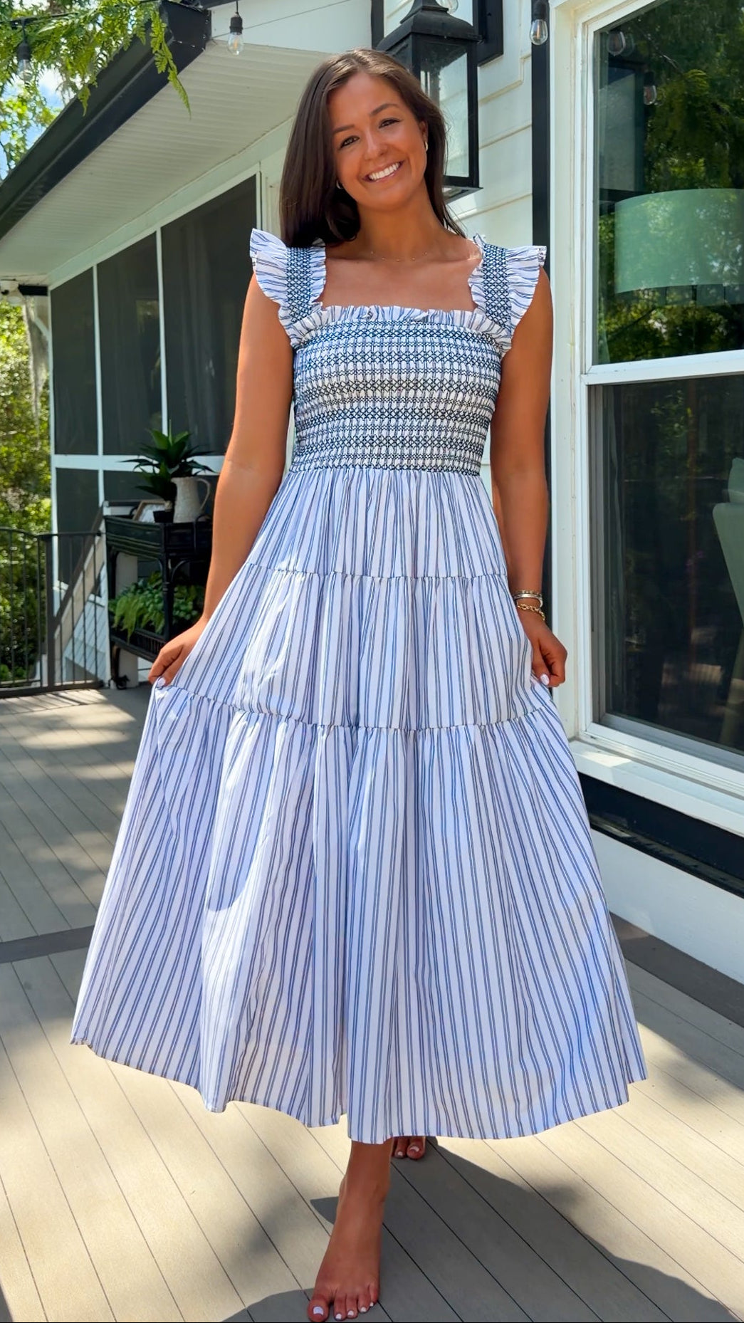 Woman wearing a blue and white striped dress standing on a porch.
