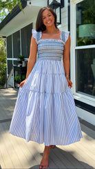 Woman wearing a blue and white striped dress standing on a porch.