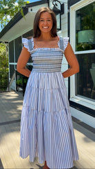 Woman wearing a blue and white checkered top and striped skirt standing on a porch.