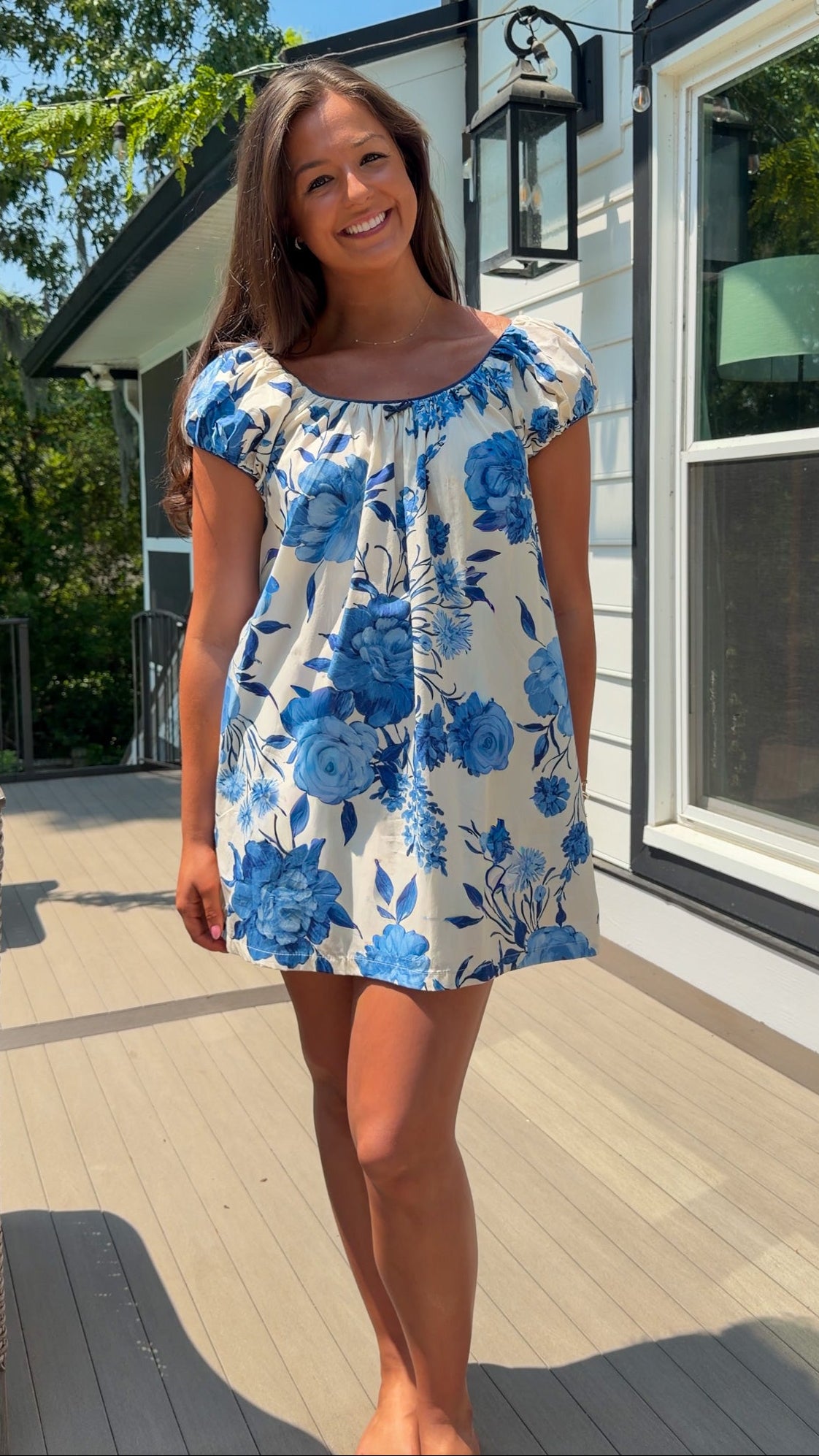 Woman wearing a blue floral dress standing on a wooden deck.