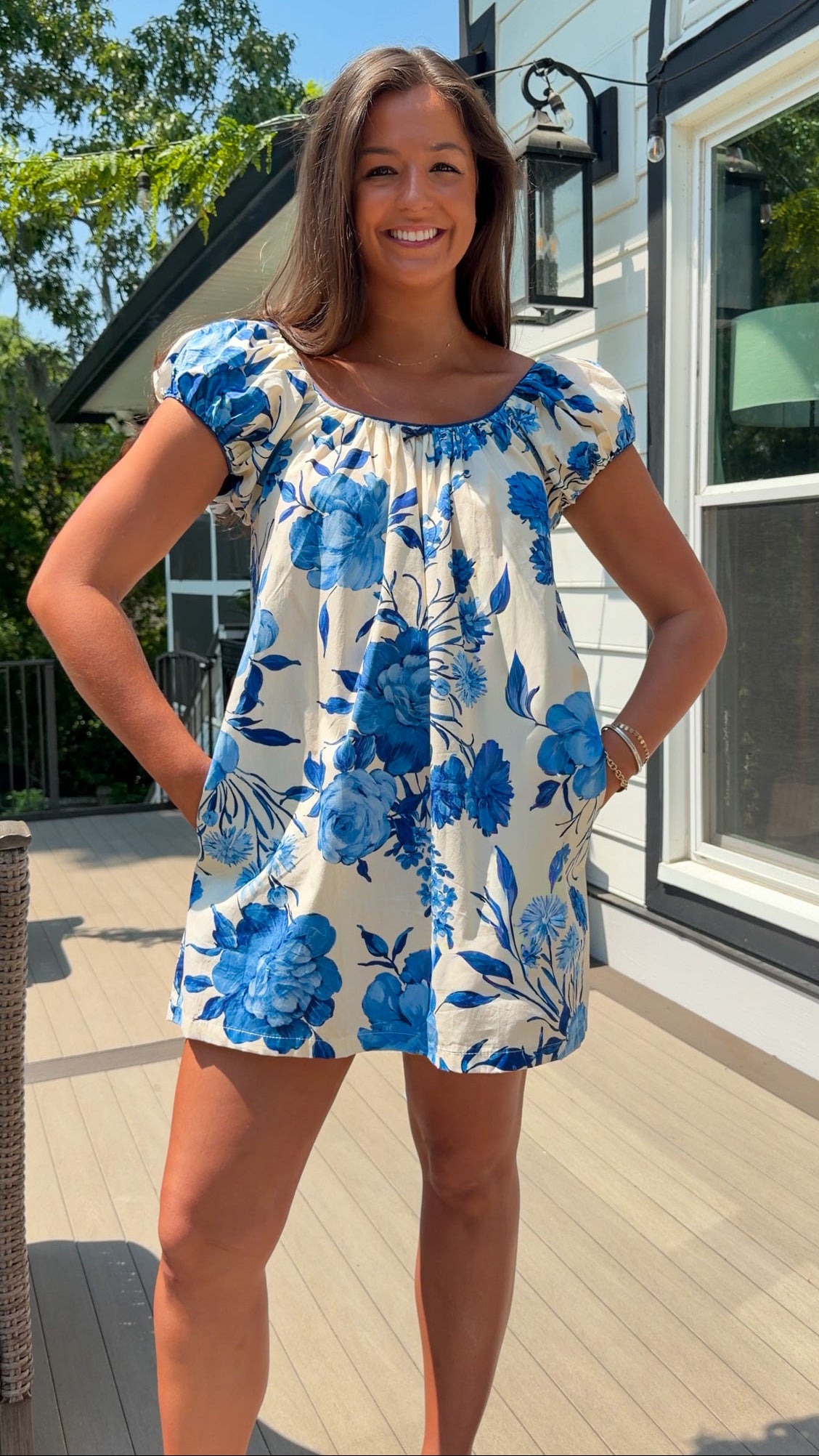 Woman wearing a blue floral dress standing outdoors on a wooden deck.