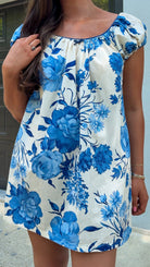 Woman wearing a blue floral dress against a light blue wall.