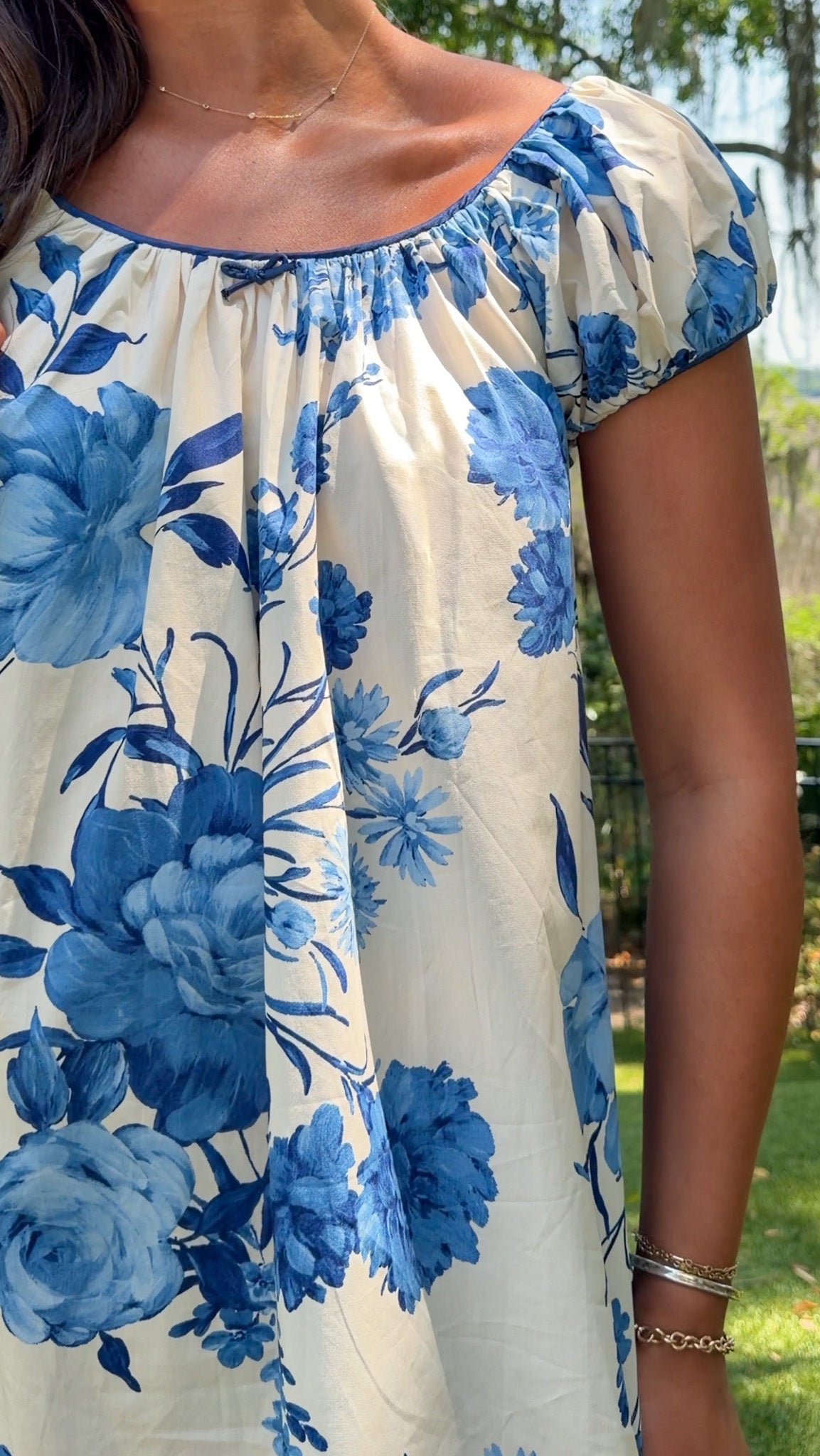 Person wearing a white dress with blue floral patterns outdoors.
