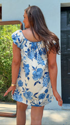 Woman wearing a blue floral dress standing outside a building.