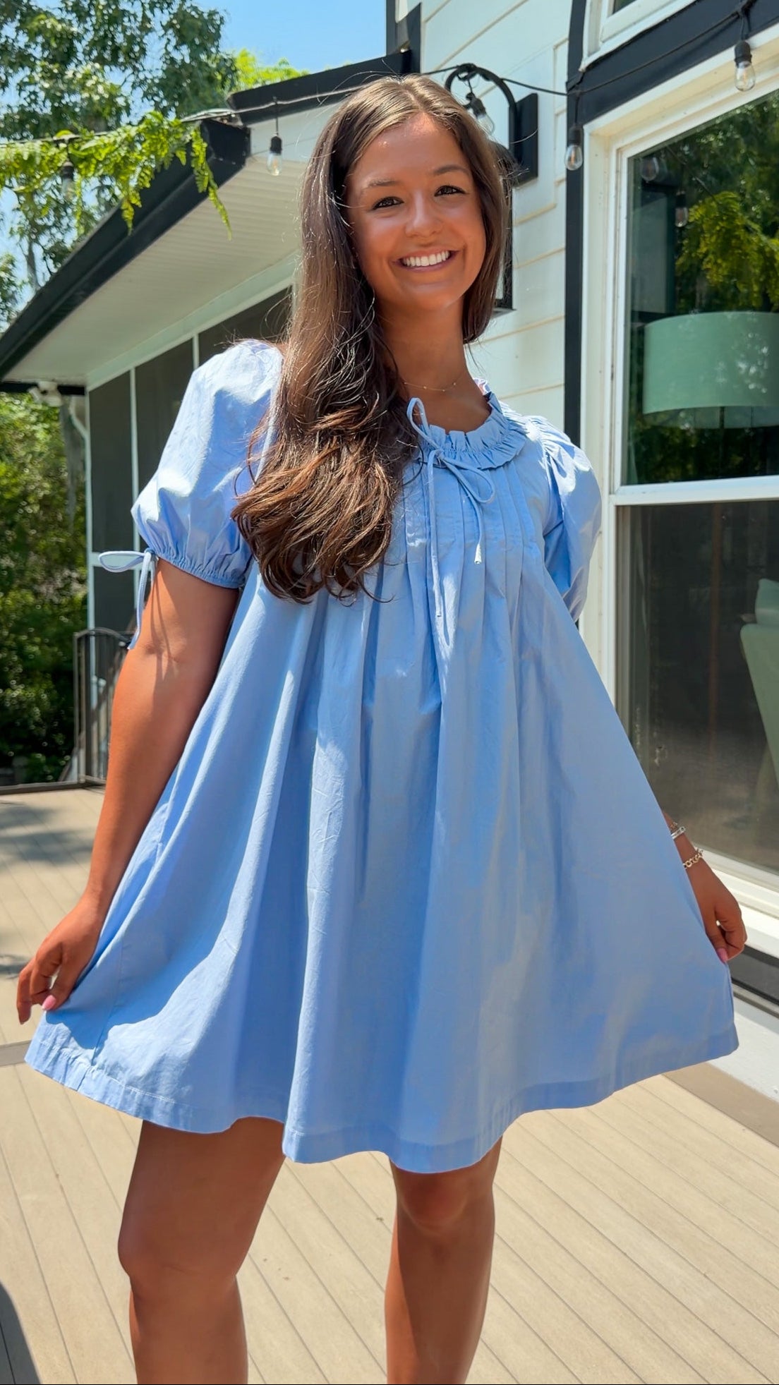 Woman wearing a light blue dress standing outdoors near a house.