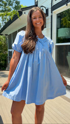 Woman wearing a light blue dress standing outdoors near a house.