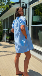 Woman in a light blue dress standing on a wooden deck with a house in the background
