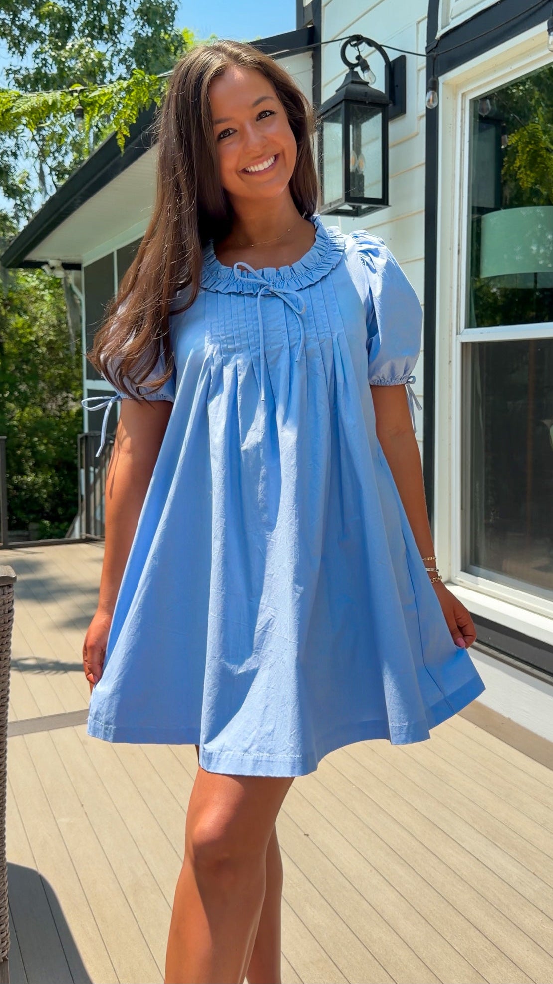 Woman wearing a light blue dress standing on a wooden deck.