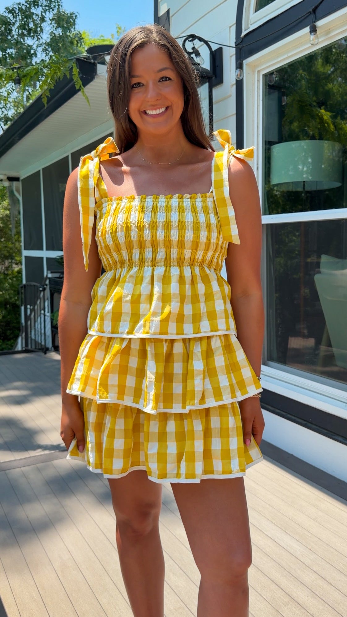 Woman wearing a yellow checkered dress standing on a wooden deck.