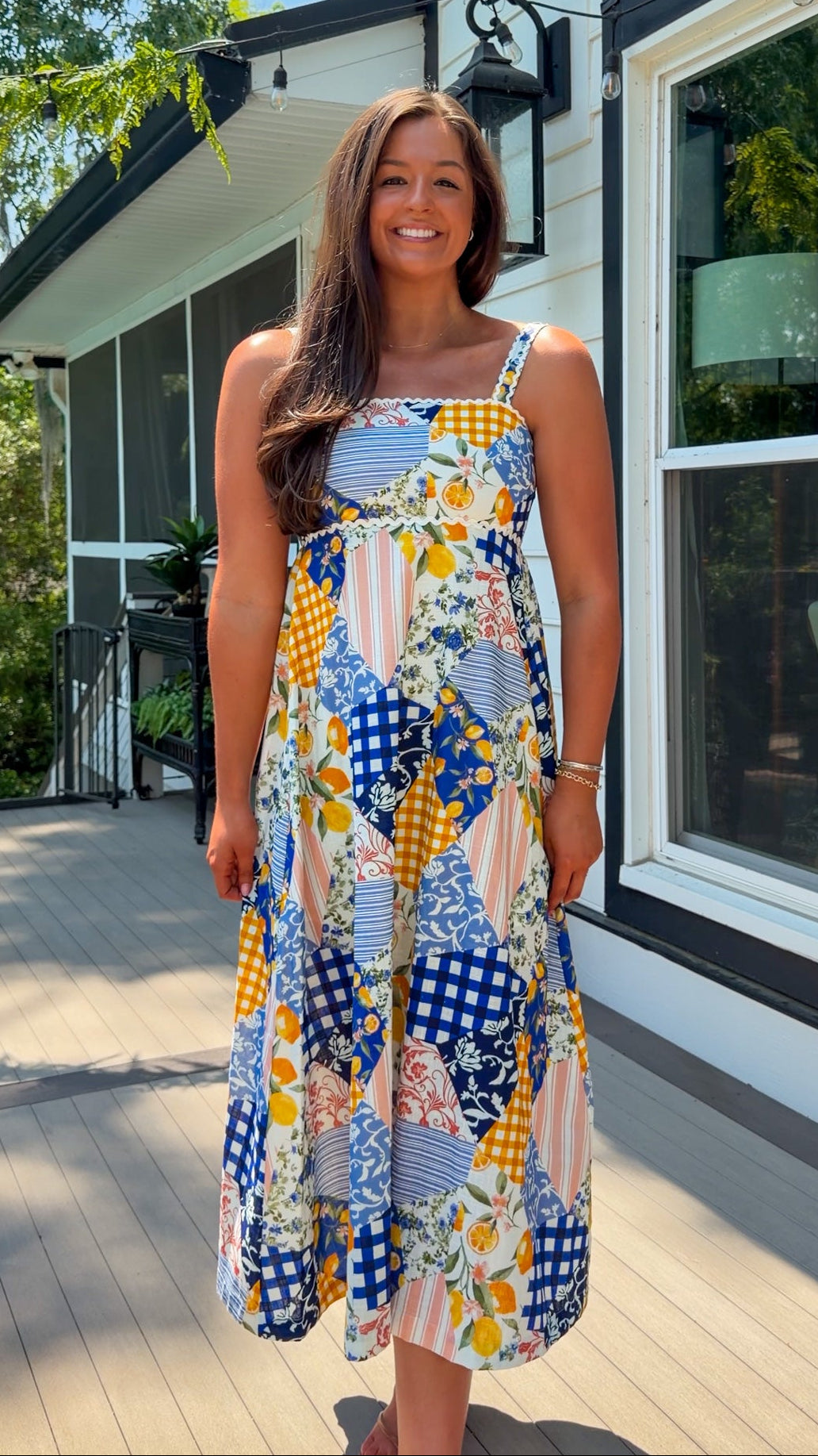 Woman in a colorful patterned dress standing on a wooden deck with a house in the background.