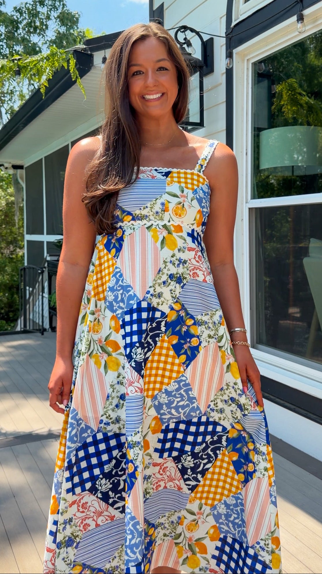 Woman wearing a colorful patterned dress standing outside a house.