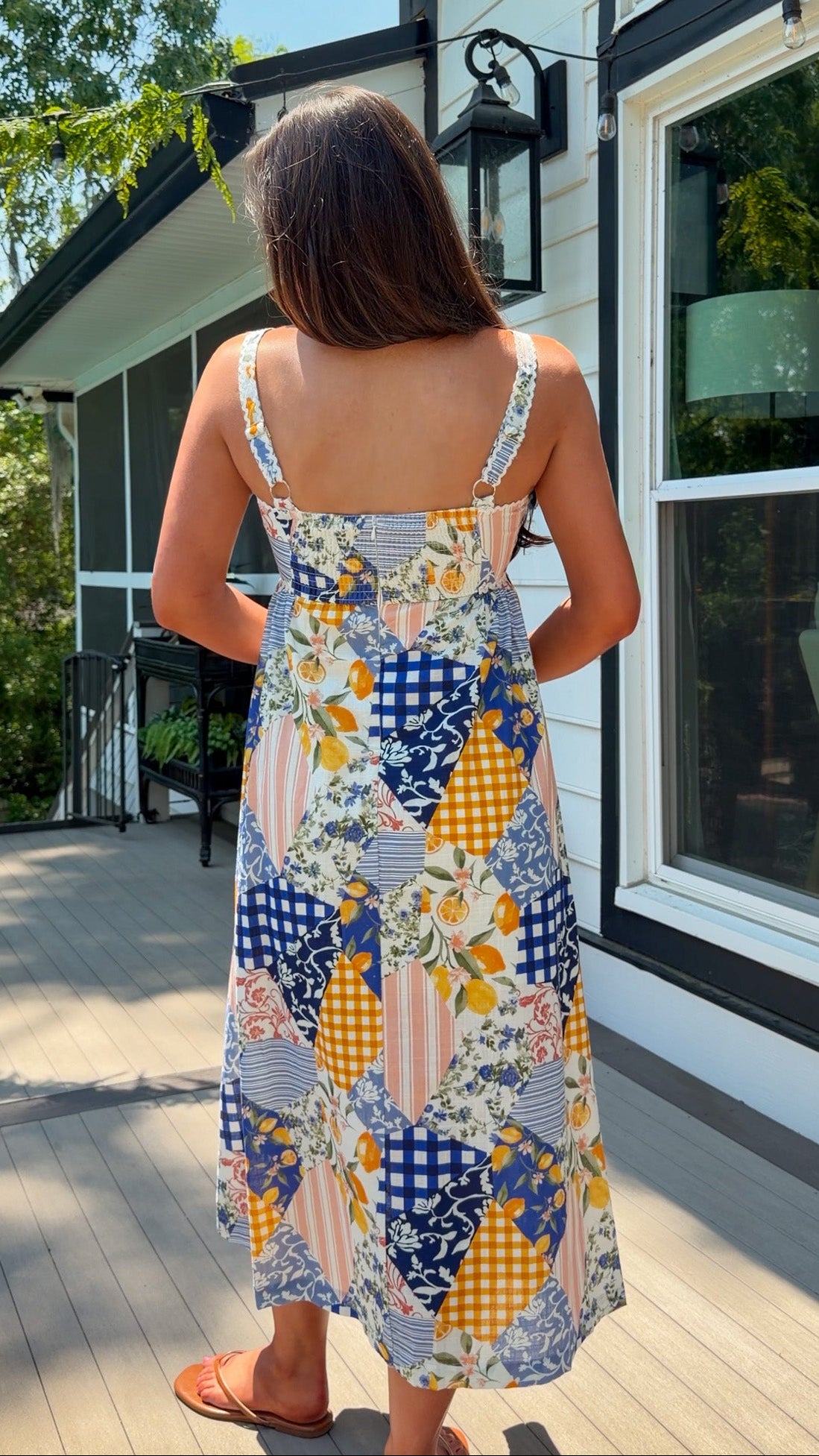 Woman in a colorful patterned dress standing on a wooden deck.