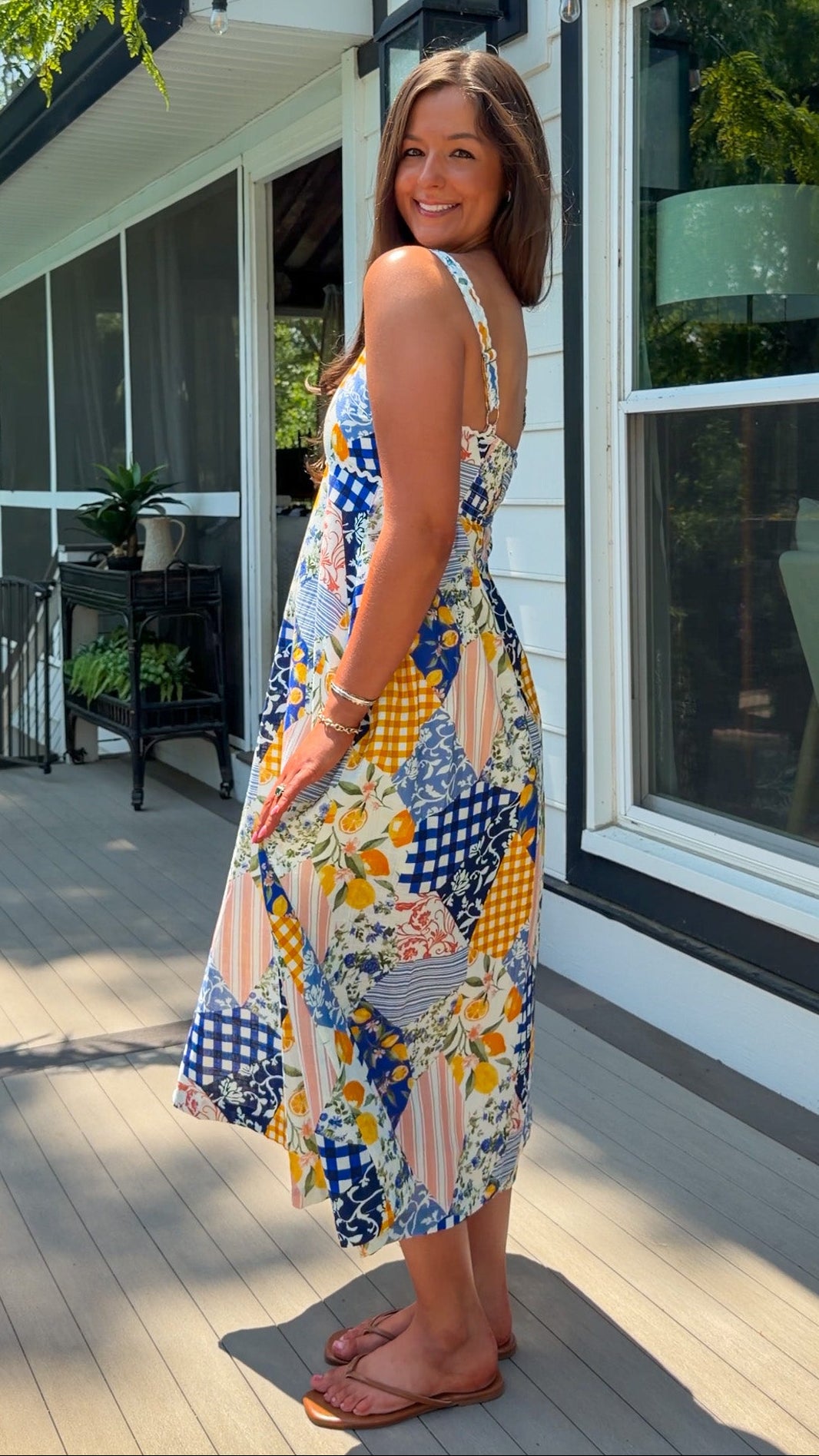 Woman in a colorful dress standing on a wooden deck of a house.