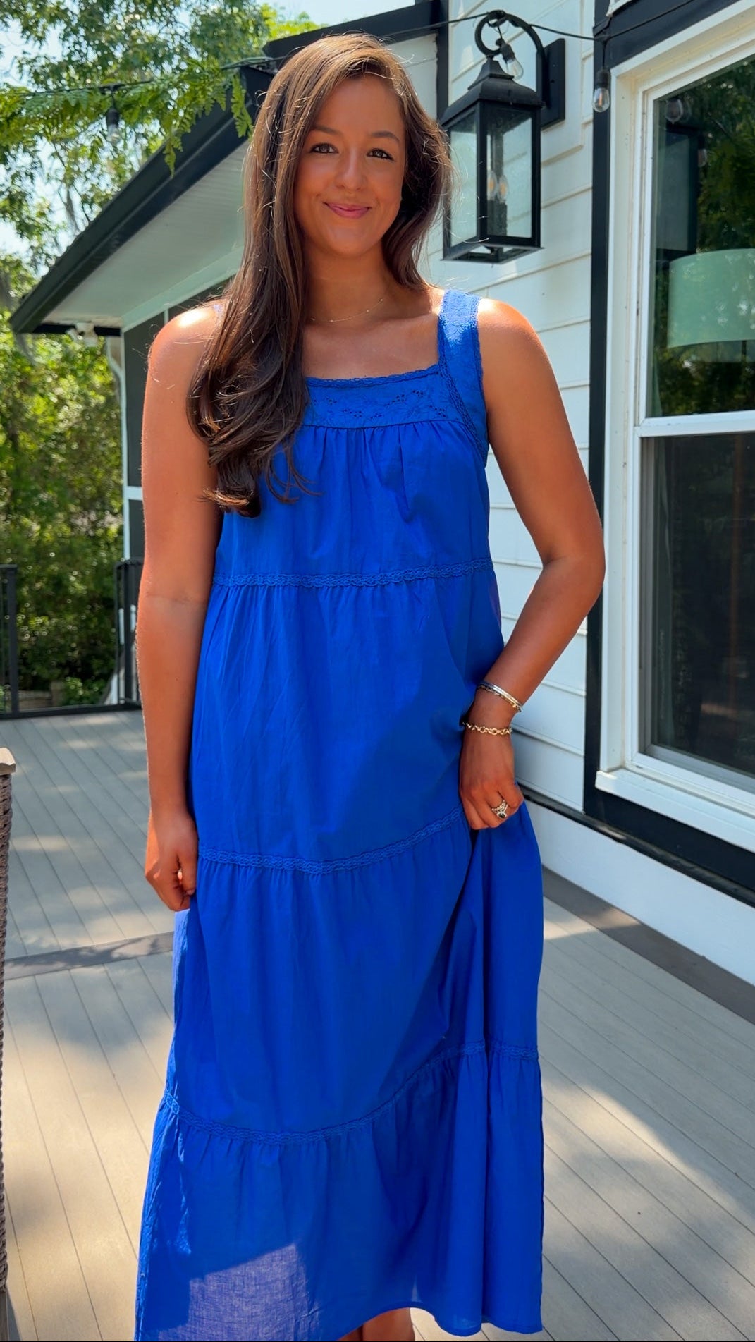 Woman in a blue dress standing on a deck with a house in the background