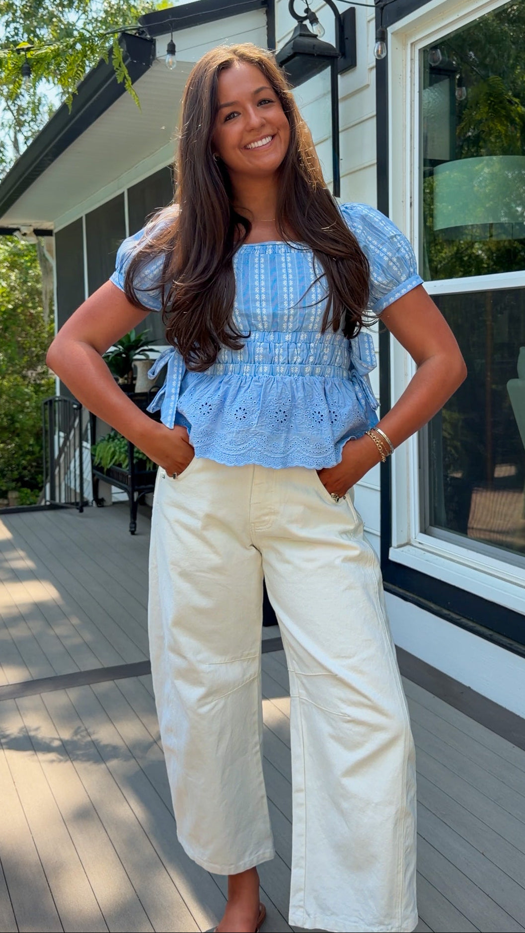 Woman wearing a blue top and white pants standing on a wooden deck.