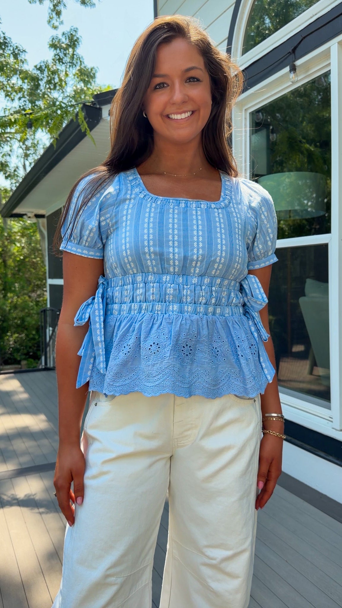 Woman wearing a blue top and white pants standing on a wooden deck.