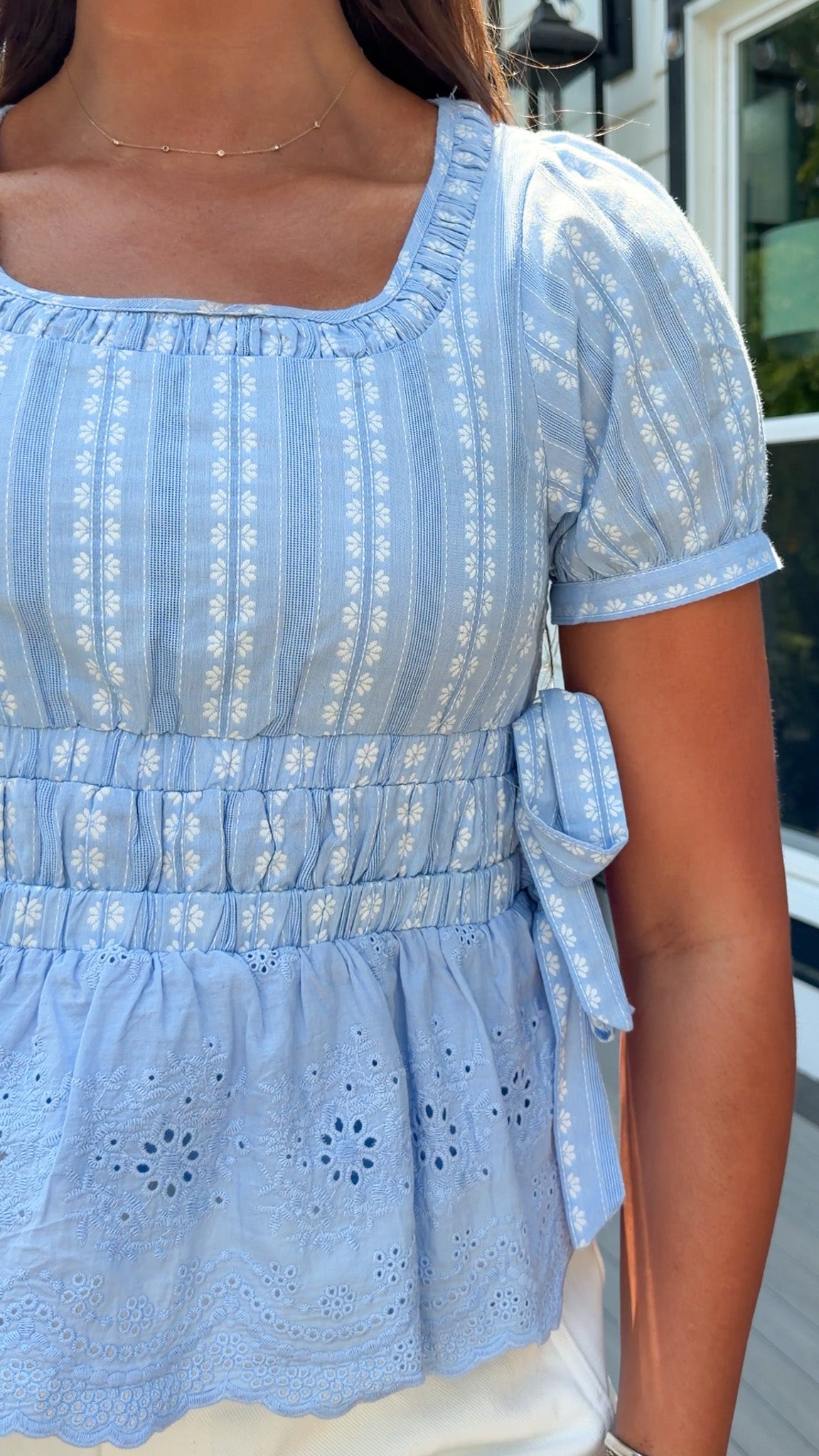 Light blue floral shirt  with white patterns worn by a person, with a blurred background.