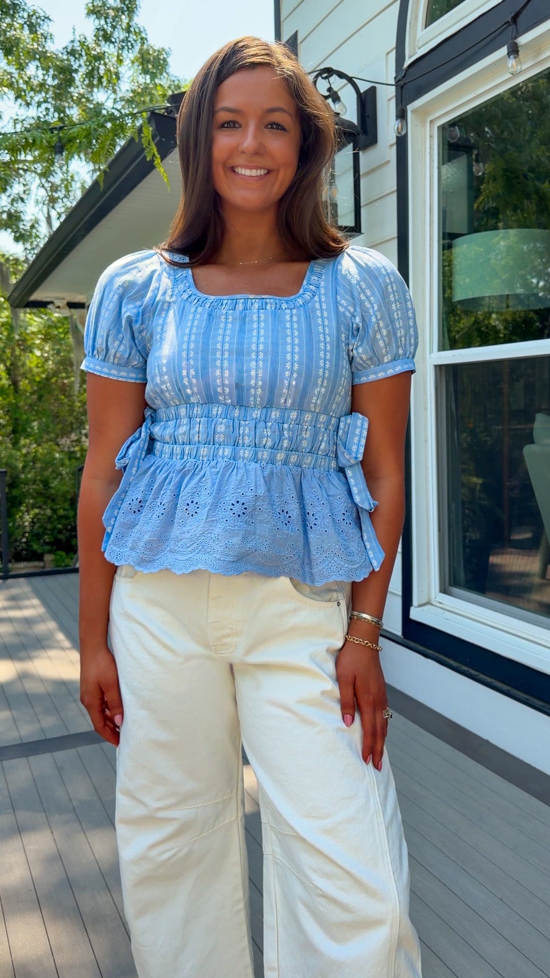 Woman wearing a blue top and white pants standing on a porch.