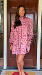 Model wearing a mauve floral corduroy babydoll dress with smocked bodice and velvet collar and cuffs standing in front of a wooden door.