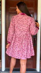 Model wearing a mauve floral corduroy babydoll dress with smocked bodice and velvet collar and cuffs standing in front of a wooden door.