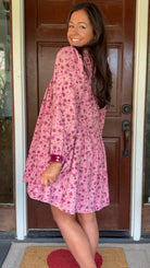 Model wearing a mauve floral corduroy babydoll dress with smocked bodice and velvet collar and cuffs standing in front of a wooden door.