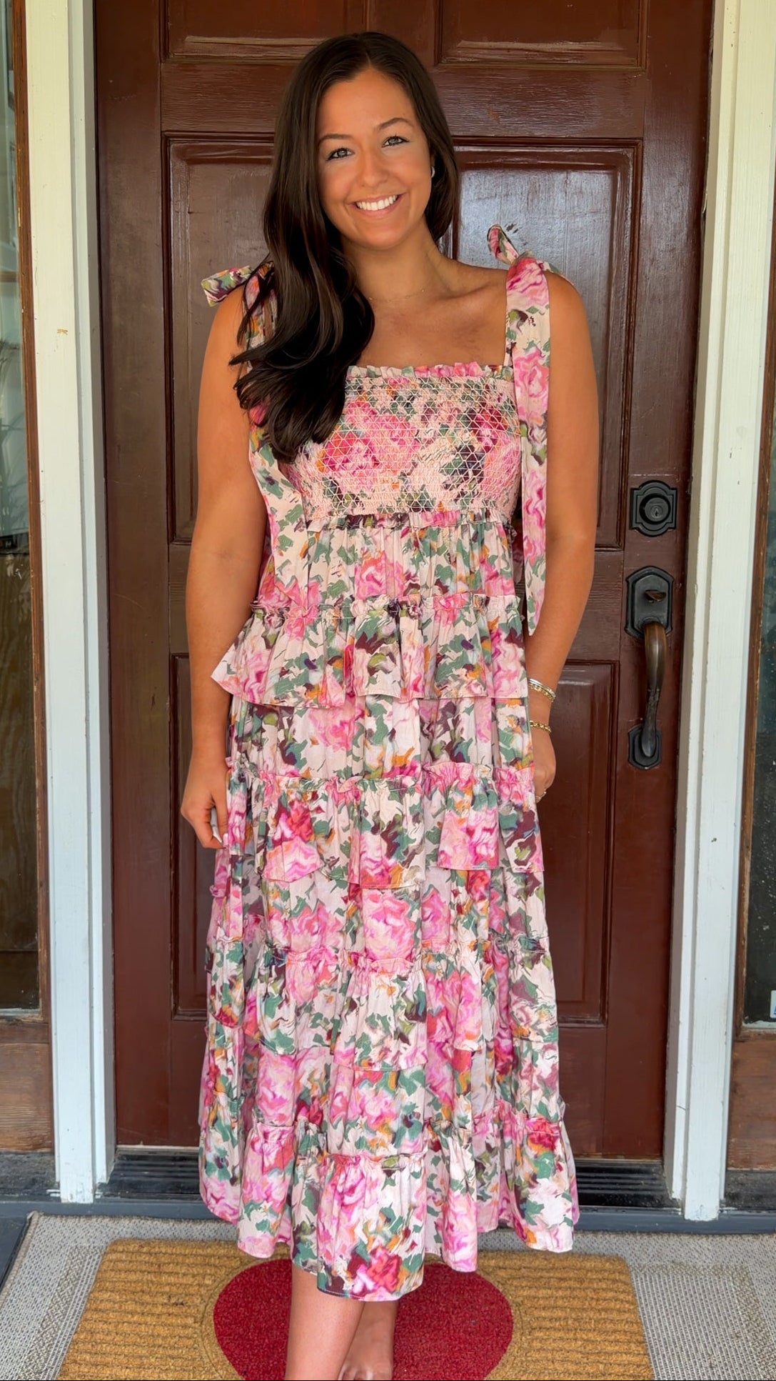 Woman wearing a floral dress standing in front of a wooden door.