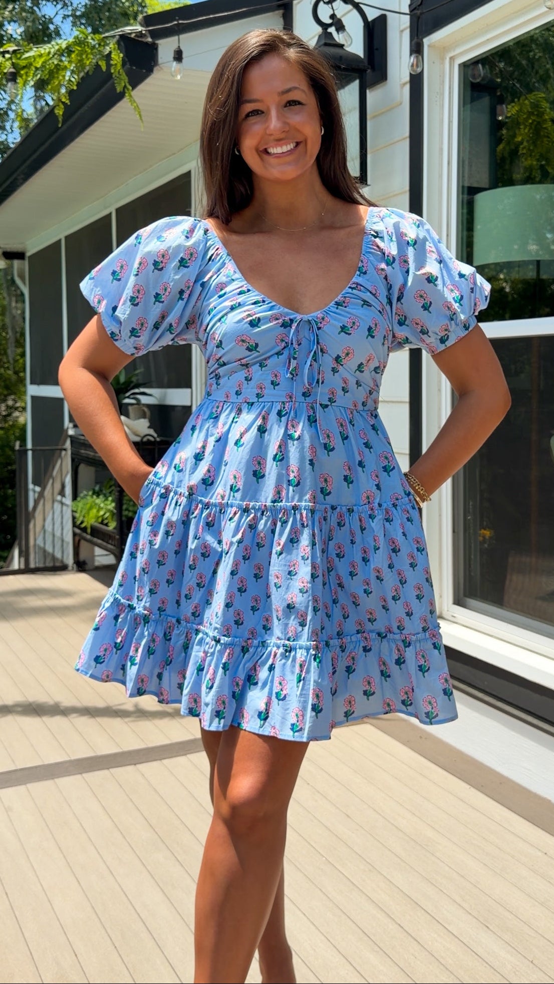 Woman wearing a blue dress with a floral pattern standing outdoors.